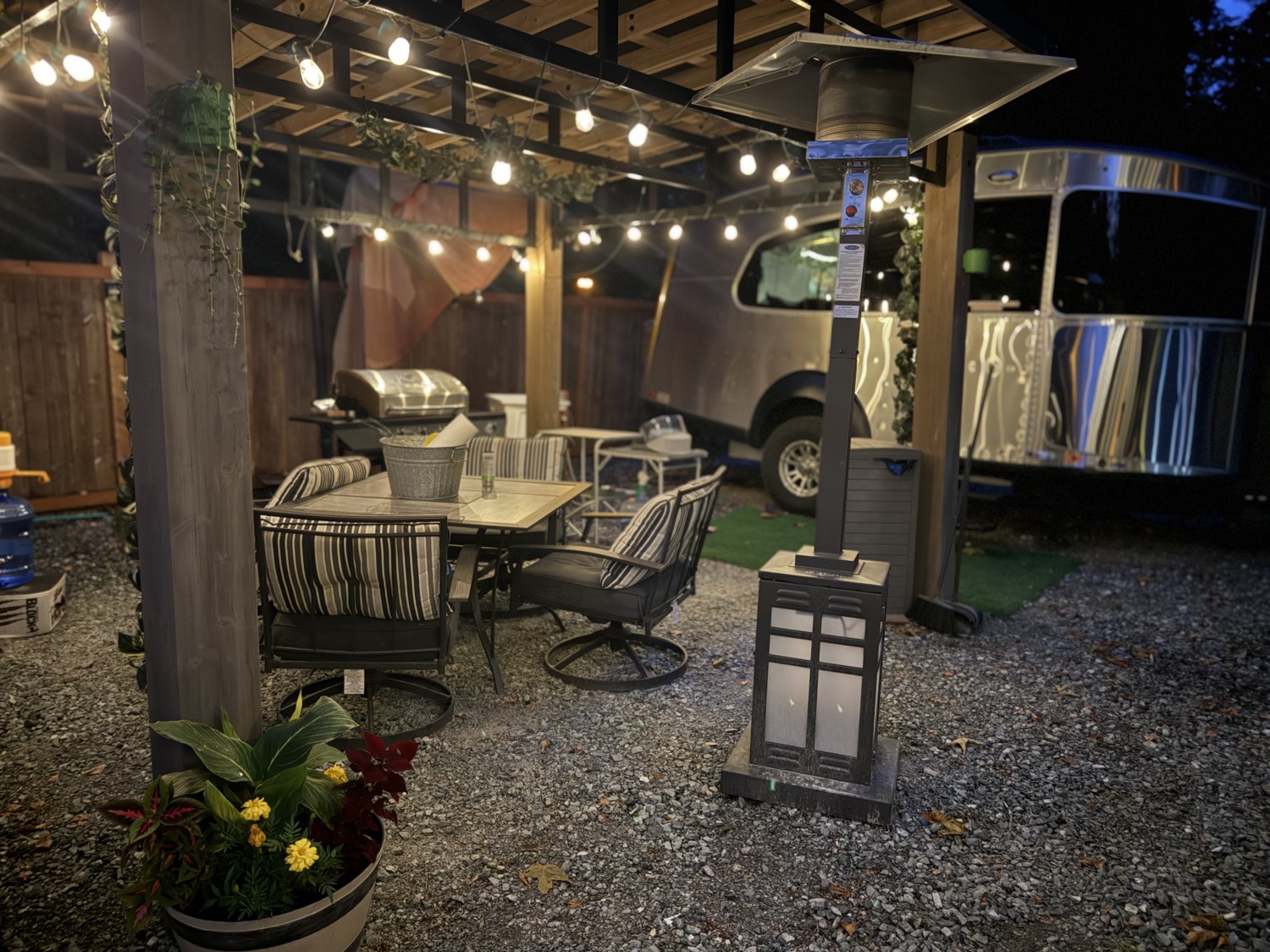 Dining table under a wood pergola with a patio heater and the silver trailer behind
