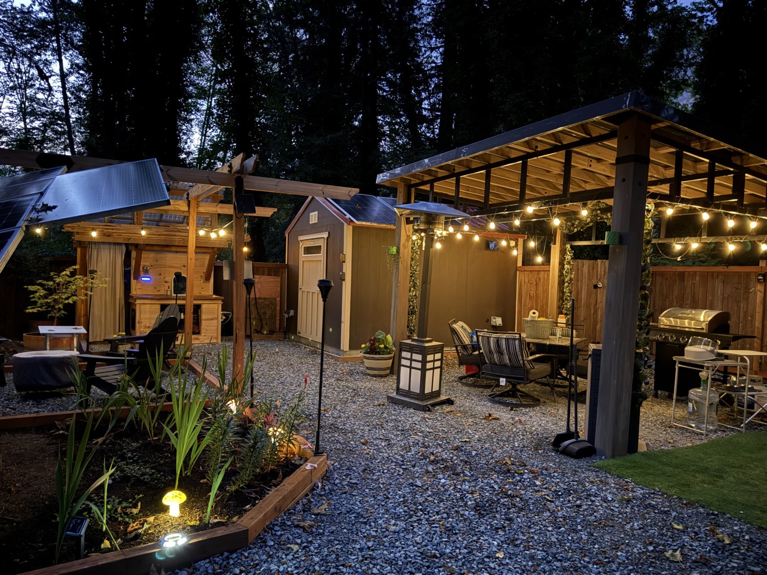 The gravel glamping site at night, with string lights, a garden, and the pergola